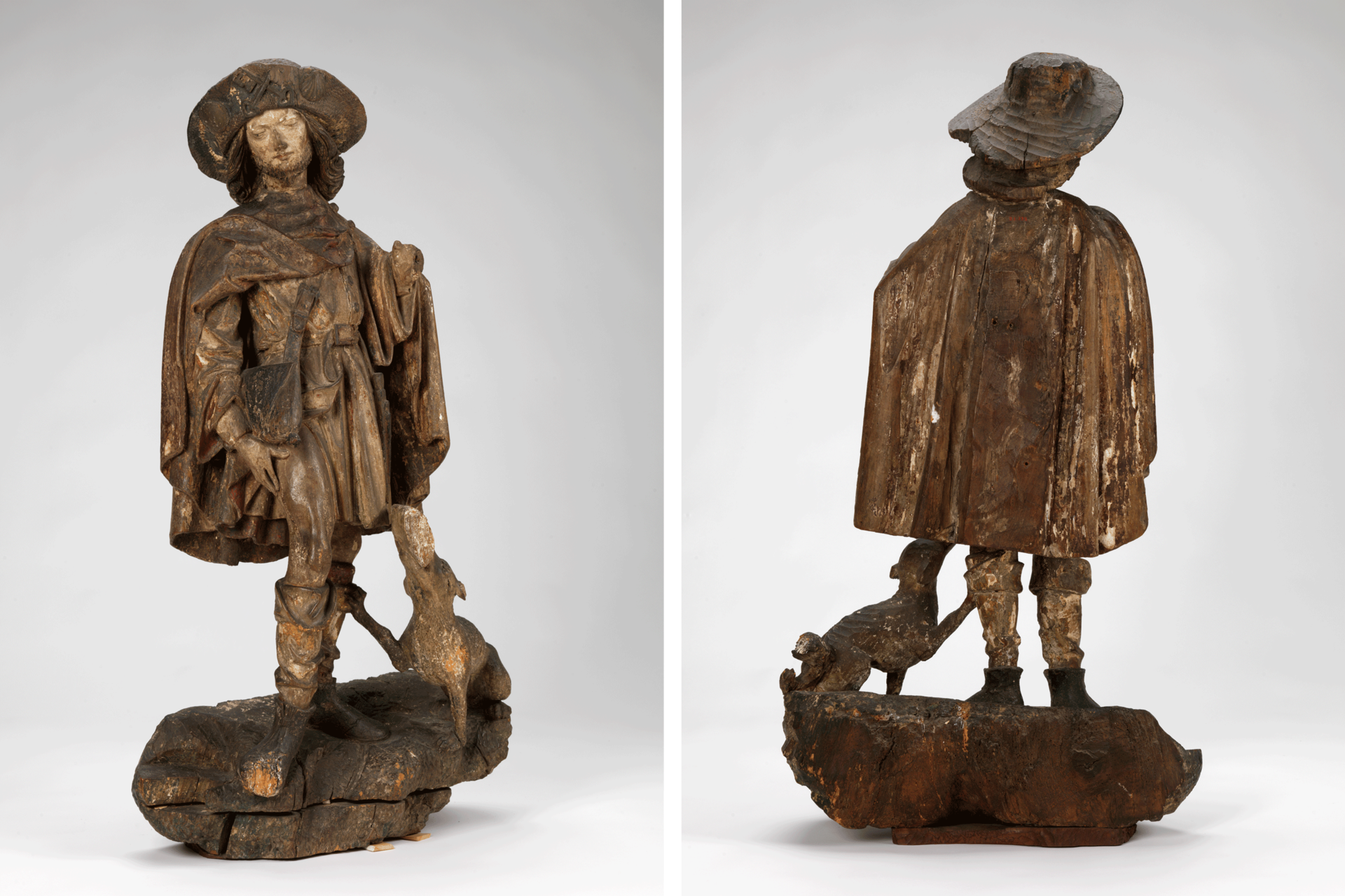 Dark-brown sculpture of a standing man wearing a cape, hat, and boots. He looks to the side, hand on his thigh. A dog at his feet looks up at him.