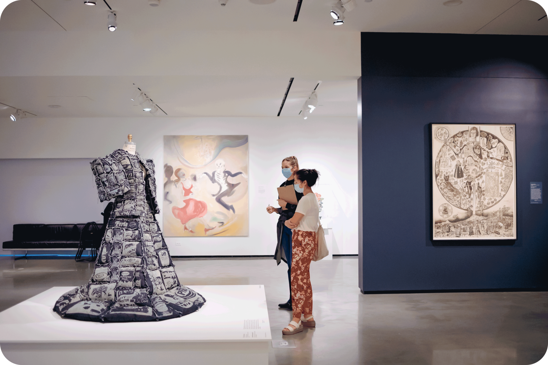 Two people looking at a mannequin wearing a bulky dress. Besides them is a blue wall featuring a monochromatic work, and behind them is a large oil painting. 