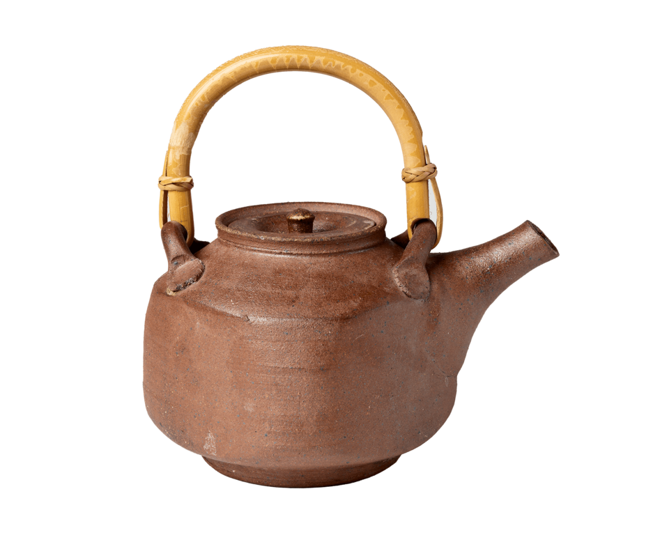Square-shaped brown teapot resting on circular foot. Rounded tan handle on top of teapot.