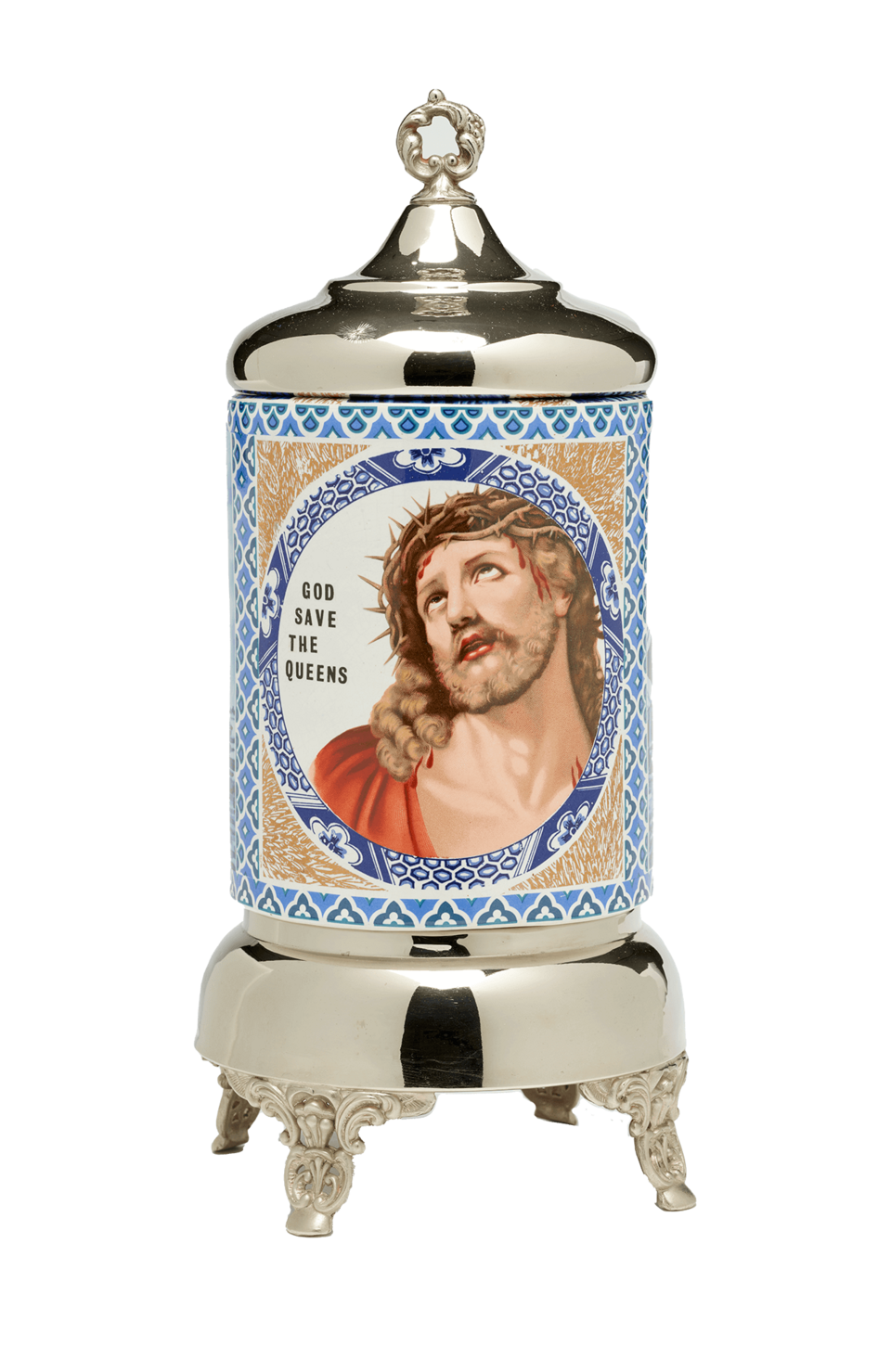 Sculpture with ceramic body covered in blue, white, and tan decoration. Image in the center of Jesus next to the words “God save the queens.” Ceramic is framed by a metal top and base on four ornate feet.