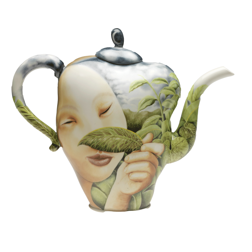 Teapot with spout facing right. It is painted with a large, light-skinned face and hand holding a green leaf partially over face, surrounded by tropical green leaves and cloudy blue sky