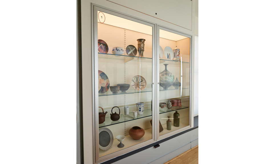 A case with four shelves is set into a wall. The shelves hold many different ceramic objects.