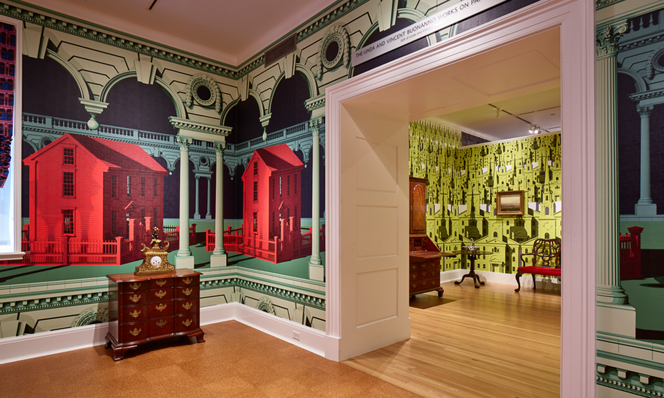 Colorful wallpaper embellishes the walls of two adjoining rooms containing antique furniture. The foreground pattern includes large vibrant red houses and green architectural details. A chartreuse pattern is adjacent.