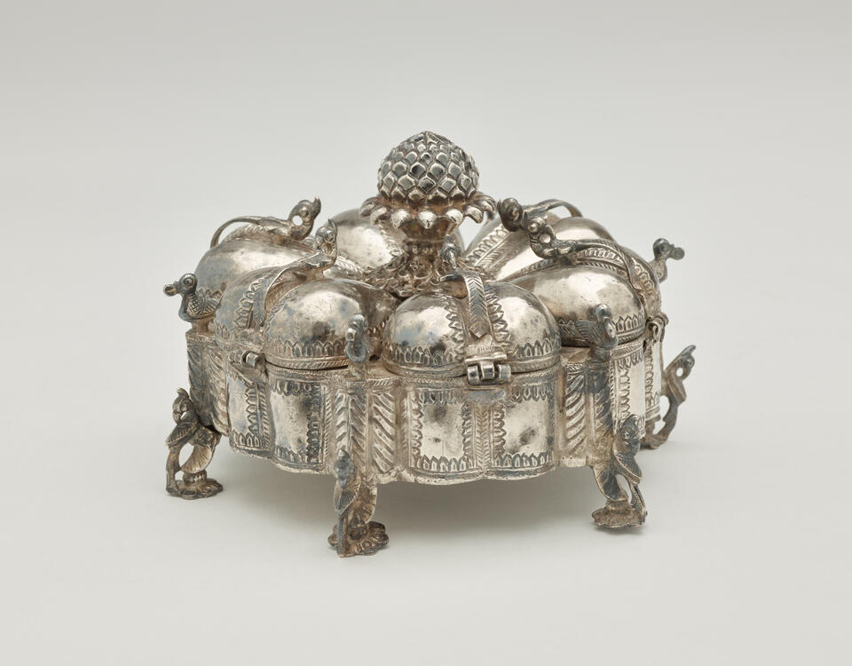 A dark silver spice box that is sculptural and has many different rounded compartments.