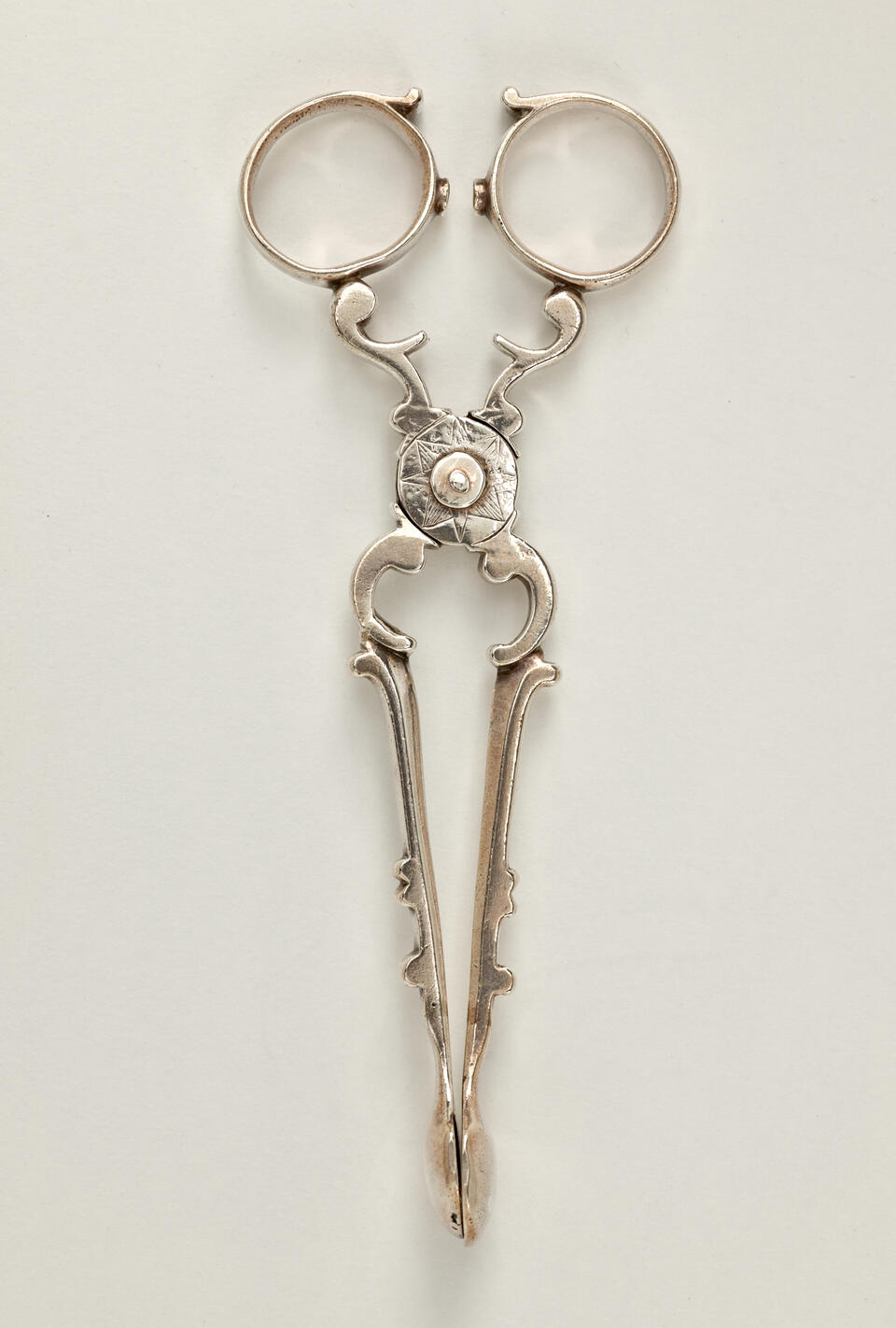 Silver sugar tongs that are delicate and swirled.