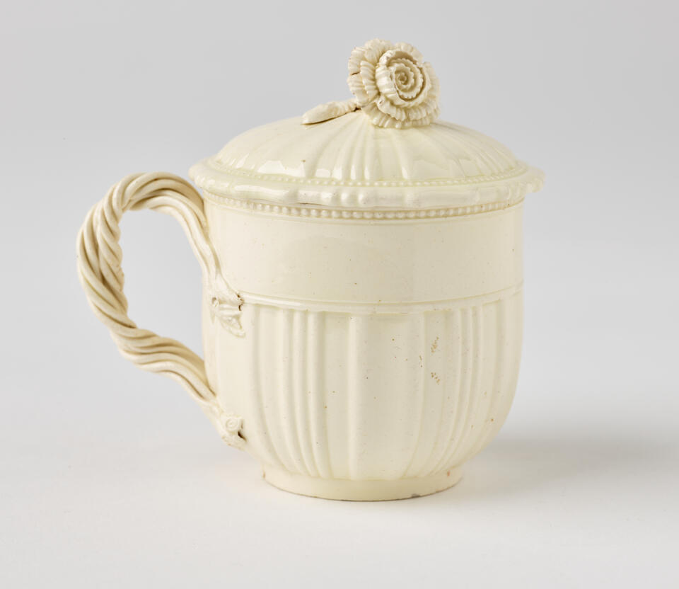 A white creamware custard cup, with a sculptural swirled handle, and lid with sculpted finial.