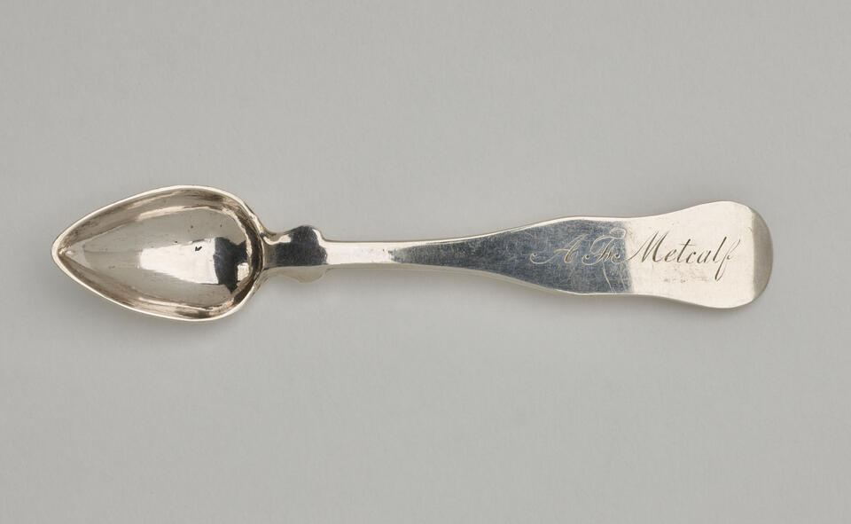 A silver salt spoon the bowl comes to a pointed tip, the neck is thin, and the handle is thicker and rounded at the end. 