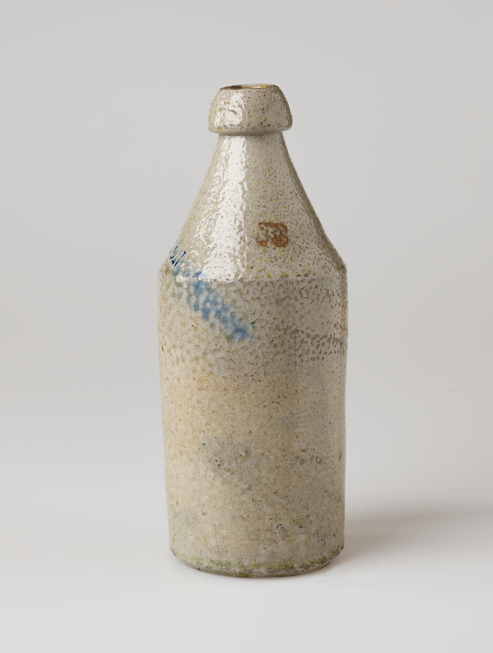 A cream ceramic bottle with a thick rounded lip tapering out to a cylindrical body. There is a dark rust colored spot and a blue line.