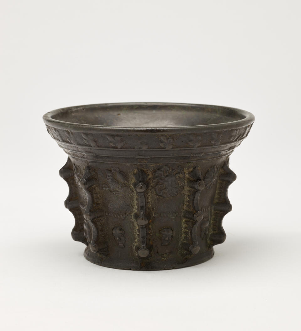 A bronze mortar with protruding decorations on the exterior. 