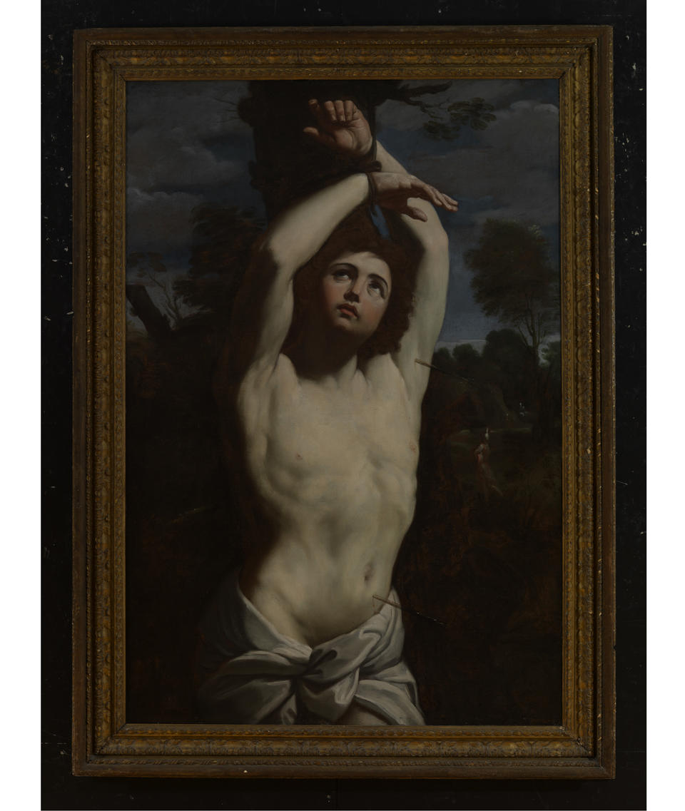 Painting of a young shirtless man, two thorns piercing his body, surrounded by a dark landscape. He looks upward at his hands, which are bound to a tree. 
