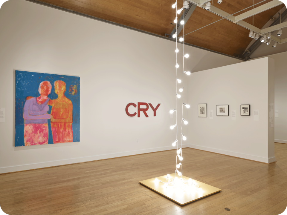 Installation view of an exhibit. Featured are a vibrant painting of two figures, an artwork spelling “CRY”, and monochromatic works. In the center space is a sculpture consisting of lightbulbs. 