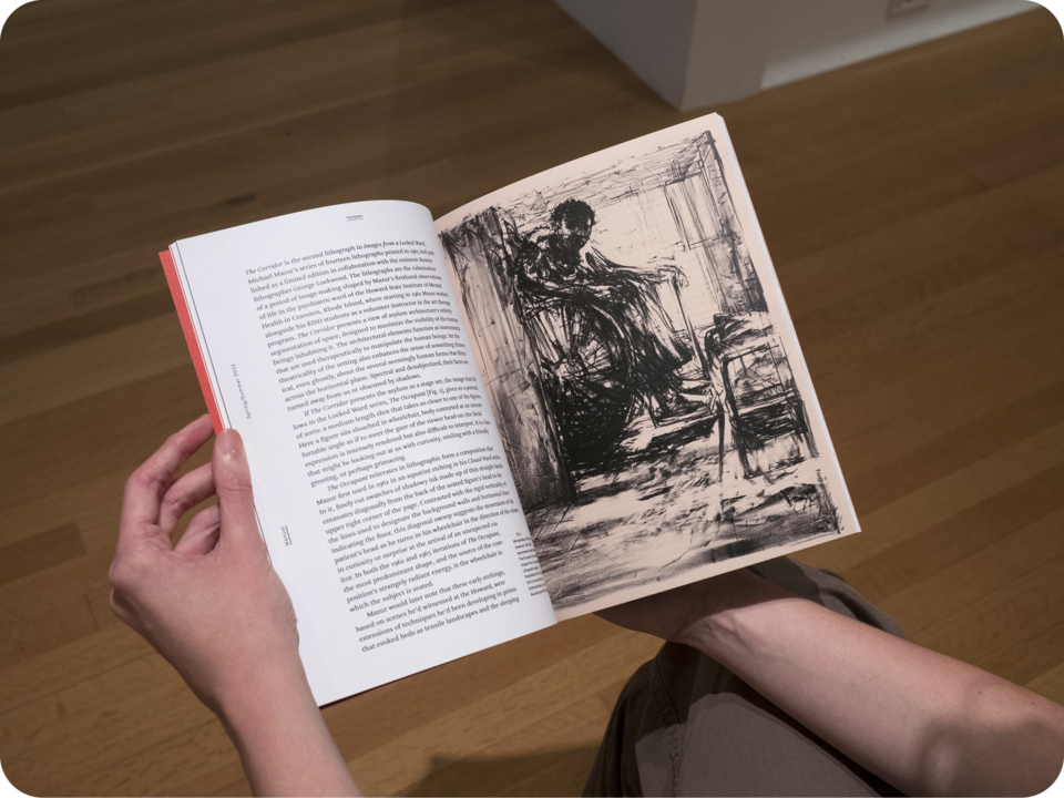 A person holding the book open. The left page features text against a white background while the right page features a black etching of a man in a wheeled chair. 