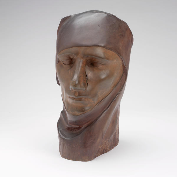 This dark brown wood sculpture presents the head of an individual of undetermined gender wearing a simple head covering that wraps around the figure’s neck.